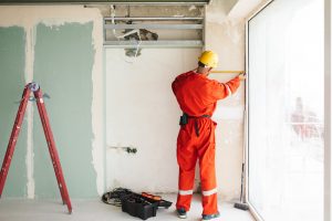 Builder in orange work clothes and hardhat using measuring tape